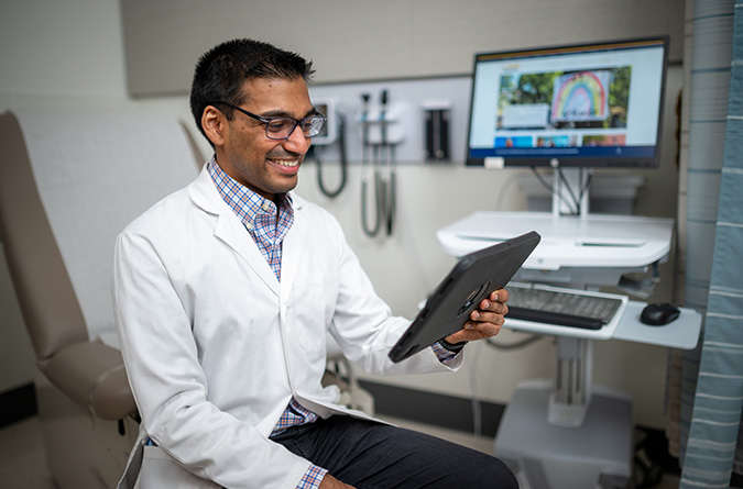 A physician smiles at a tablet device during a telehealth appointment.