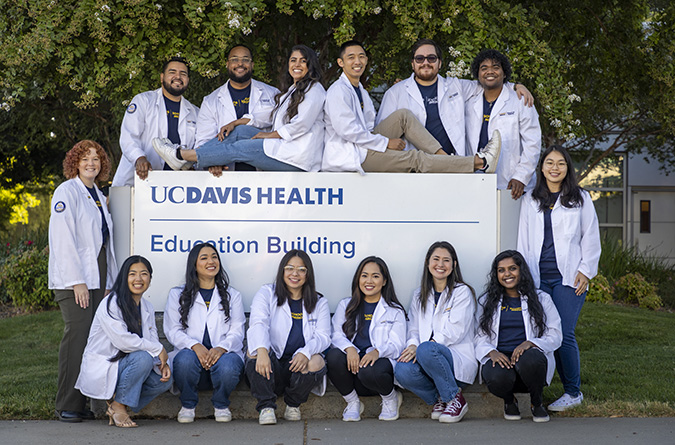 Diverse medical students gather around the UC Davis School of Medicine sign