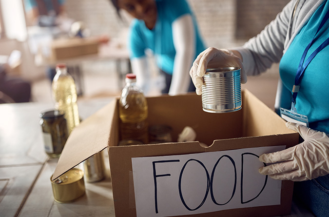 A woman adds a can of food to a box labeled "food" to donate. 