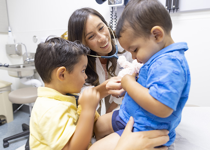 A physician smiles while caring for two pediatric patients during an appointment.