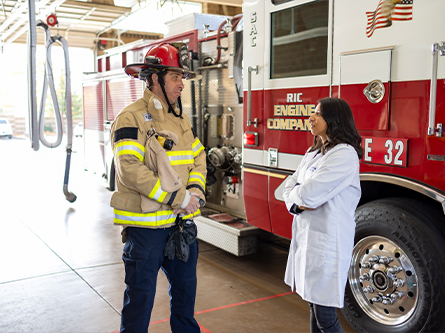 Firefighter speaking with professor and associate director for Population Sciences beside a fire truck