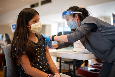 Teen girl receiving a vaccination from a health care worker.