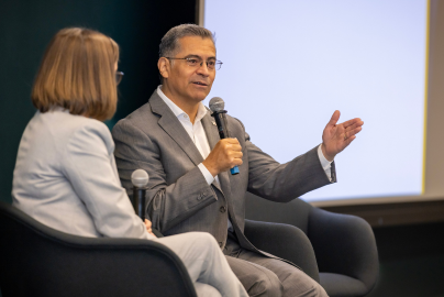 Courtney Lyles and Xavier Becerra sit on a stage holding microphones while in conversation.