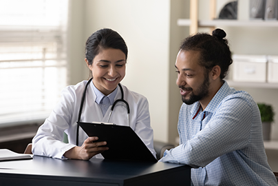 Doctor pointing to clipboard, talking to smiling patient