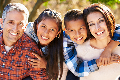 A family of four with their arms around one another, smiling. 