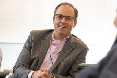 Josh Fenton sits and smiles in a dark suit jacket over a light shirt.