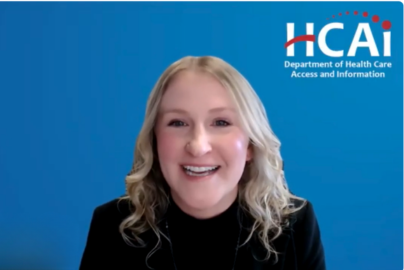 A woman with blonde hair wearing a dark shirt speaks in front of a background with the HCAI logo.