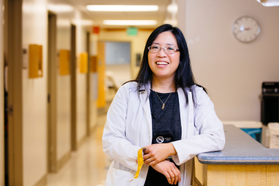 Elisa Tong smiles in a hospital hallway wearing a medical coat.
