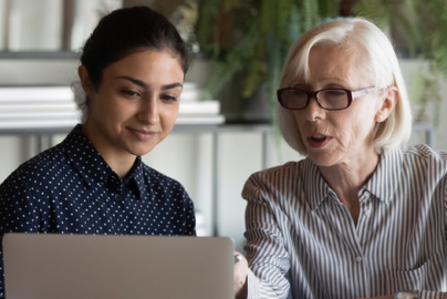 An older and a younger woman look at a computer screen together.