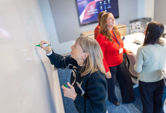 A group of women in a conference room with one writing on a white board. 
