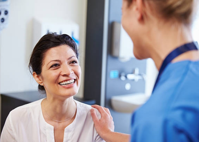 A doctor in blue scrubs talking with a patient in an exam room.