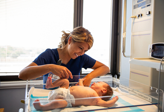 Health care provider smiling down on newborn in hospital room.