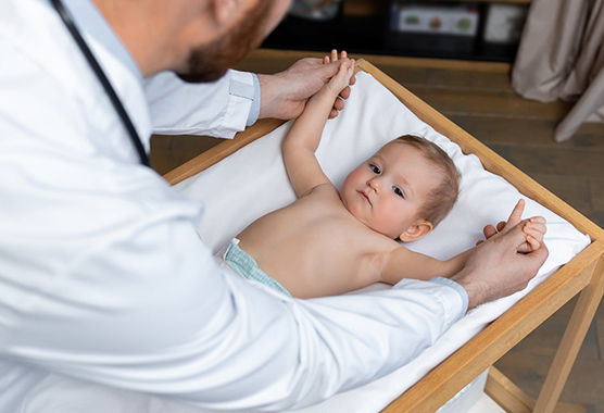 Pediatrician holding baby’s hands on the table while discussing inguinal hernia and hydroceles.