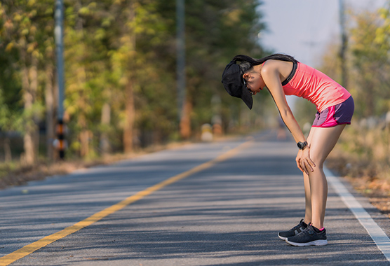 Female runner bent over on a trail in pain from an overuse injury.