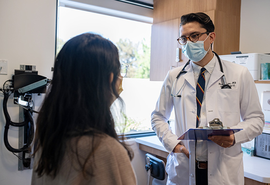 A doctor holding a clipboard speaks to a female patient.