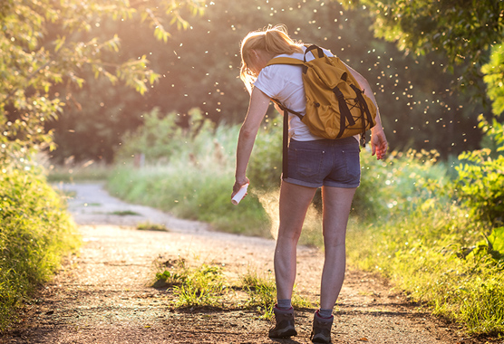 Woman out hiking stops to spray herself with bug repellent.