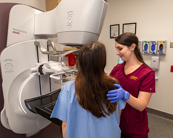 A female technician positioning a woman at an imaging machine to receive a mammogram.
