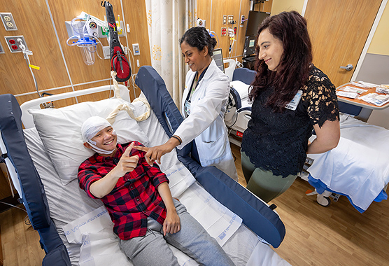 Male patient hooked up to an EEG monitor while doing a test with two health care providers all smiling.