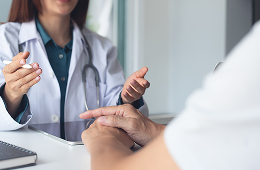 A female doctor sits at a desk and speaks with a patient about their medical history. 