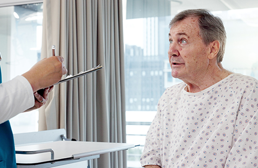 Male patient in hospital gown talking to health care provider before urodynamic testing.