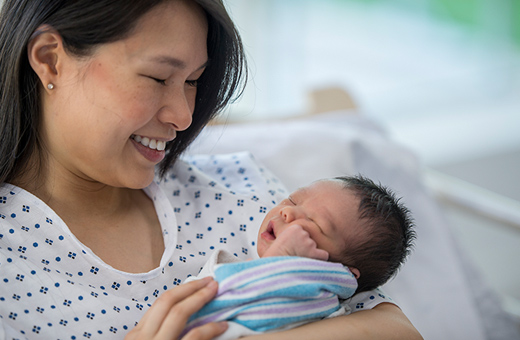New mom with newborn baby in hospital bed preparing to breastfeed.