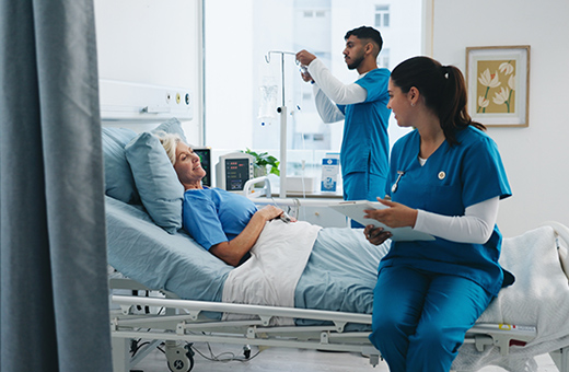 Patient in a hospital bed with two health care providers talking care after esophagectomy.