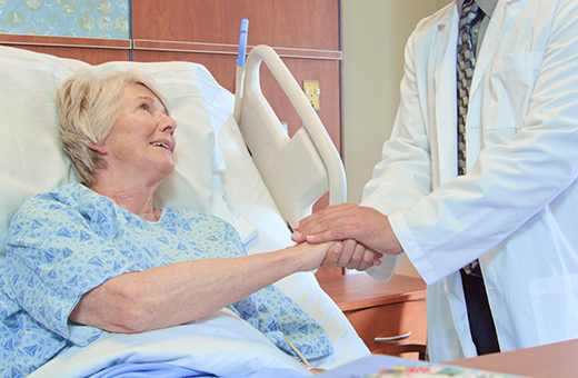 Woman in hospital bed having having knee replacement holding hands with surgeon.