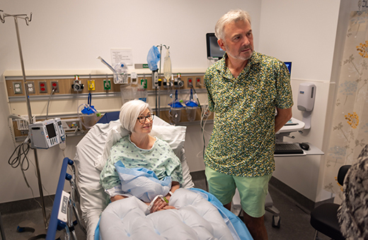 Woman preparing for knee replacement surgery in hospital bed with man standing next to her.