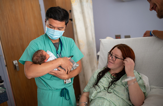Woman watching newborn baby being held by doctor in the delivery room.