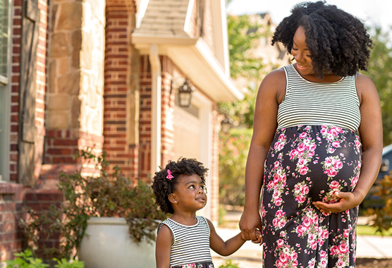 Pregnant woman walking with young daughter holding hands.