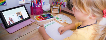 A child’s hands seen painting on paper with iPad next to them.