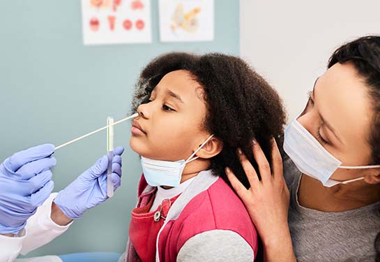A young girl gets a nasal swab for a COVID-19 test at the doctor’s office with her mom. 