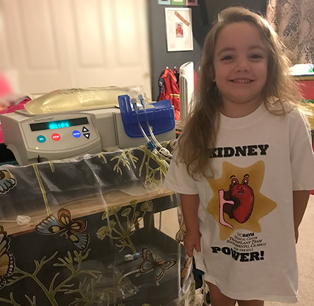 Young patient wearing a nightshirt 'kidney power' standing next to a dialysis machine
