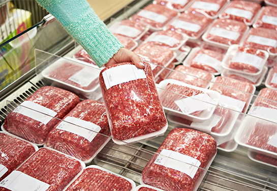 Ground beef packs in grocery store, with a woman’s hand reaching for a packet and picking it up.