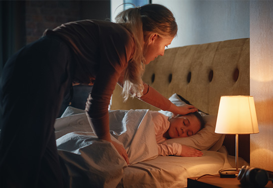 Woman touches girl’s head while she is sleeping in bed.