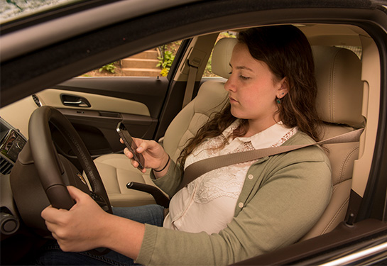 Teenager behind the wheel of parked car looking at cellphone  