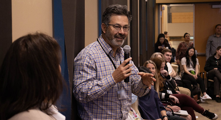 A man with brown hair holds a microphone to ask a question during a lecture.
