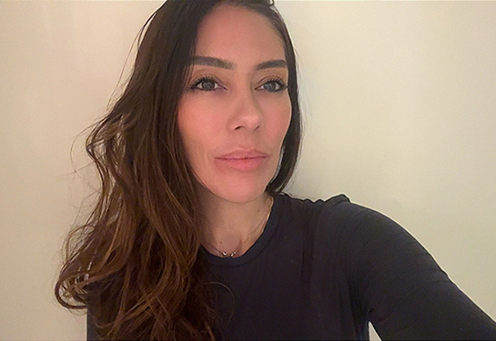 Angela Robertson, with long brown hair, wearing a black shirt, looks slightly to her left - just off camera. 