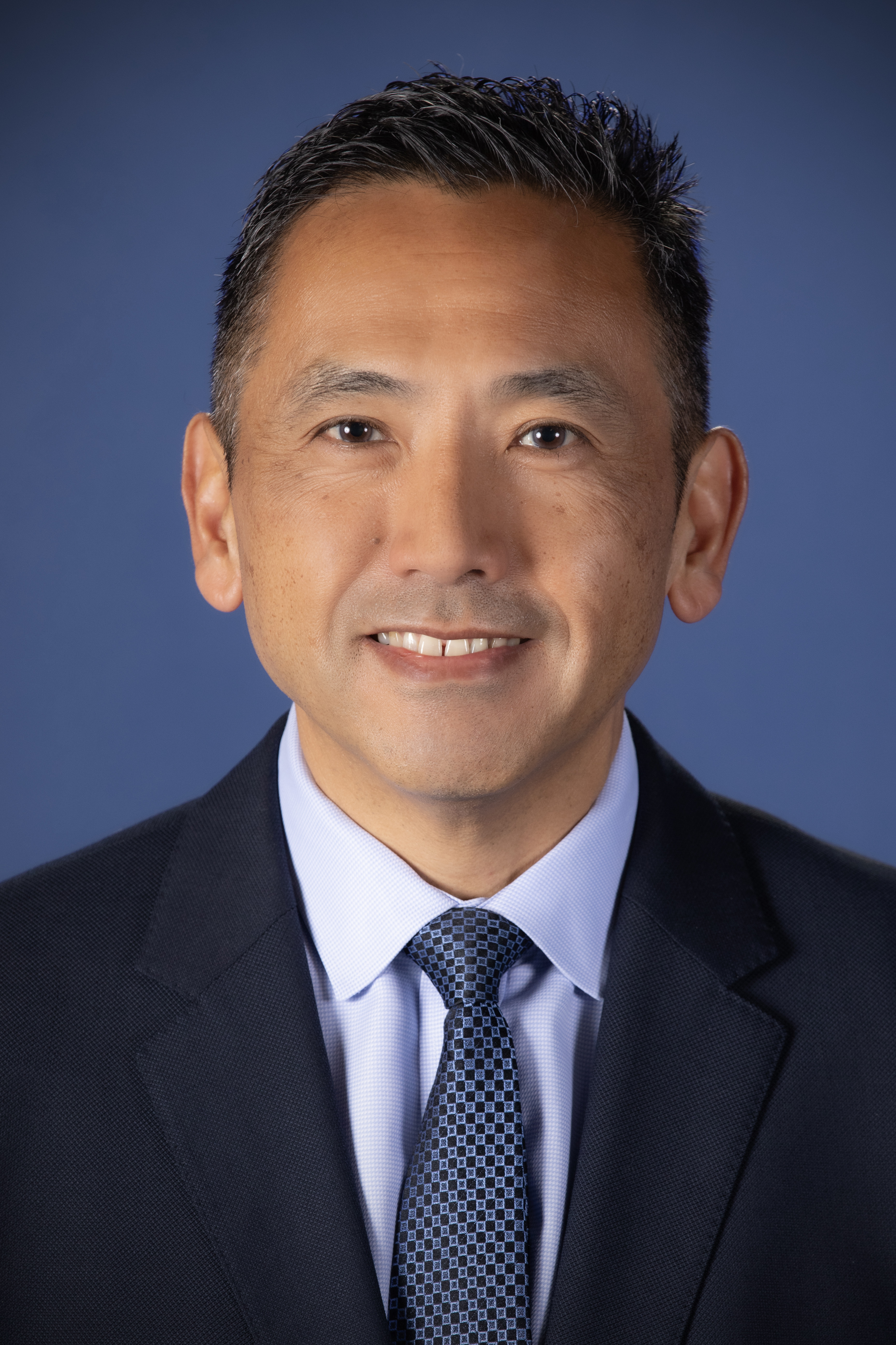 A man wearing a black suit and tie smiles for a portrait