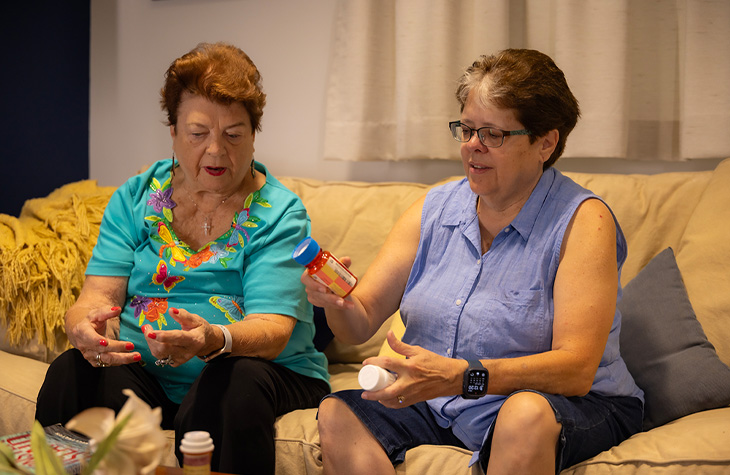 A mother and daughter review prescription medications while seated together on a couch.