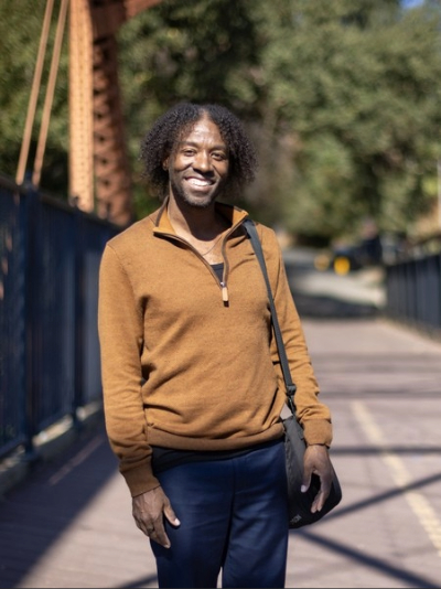 William Anderson poses on a bridge surrounded by greenery during an outdoor walk. 
