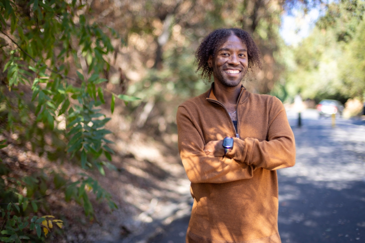 William Anderson stands on a tree-lined path outdoors near a pedestrian bridge.