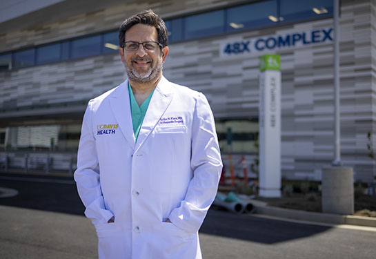 Safdar Khan, in a white doctor's coat, stands in front of the 48X building at UC Davis Health.