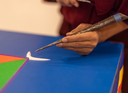Close up on sand mandala. Bright orange, green and blue colored sand placed on the artwork.