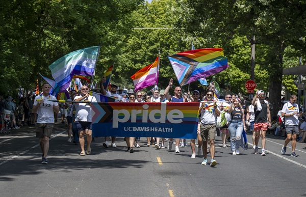 UC Davis Health employees carry a Pride banner while marching with rainbow flags on a city street.