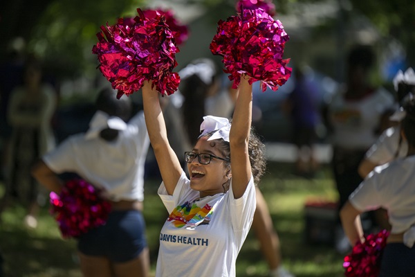 UC Davis Health participant raises pink pom-poms while wearing a Pride T-shirt during a Pride celebration.