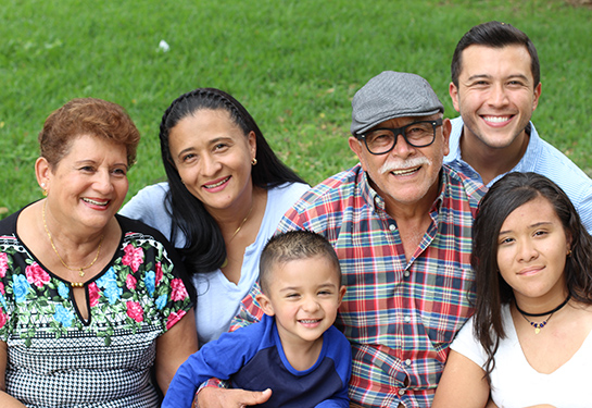 Familia hispana de seis: abuelos, padres, una niña y un niño con un fondo de zacate