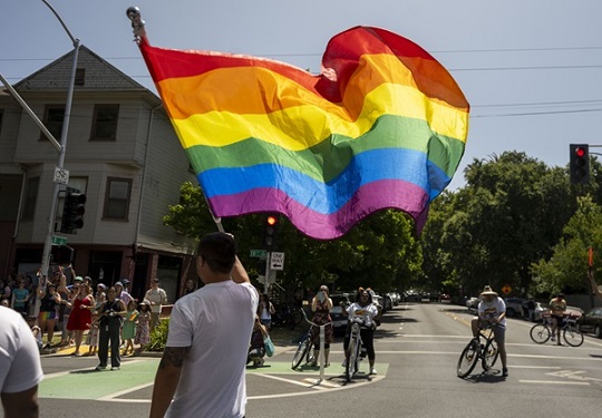 A rainbow pride flag flows in the wind as it is held by a marcher in the 2025 Sacramento Pride March