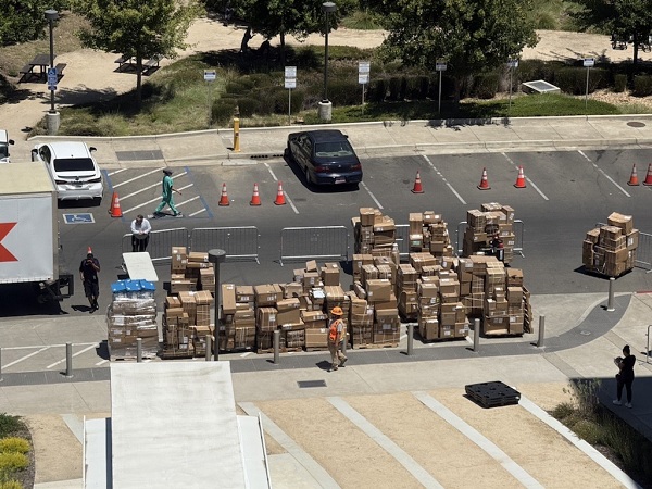 Aerial view of a loading and staging area with pallets and boxes of medical supplies arranged in rows near a truck and traffic cones.