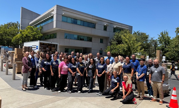Group of employees and volunteers standing outside North Addition Office Building in front of stacks of boxed medical supplies and a delivery truck after unloading supplies